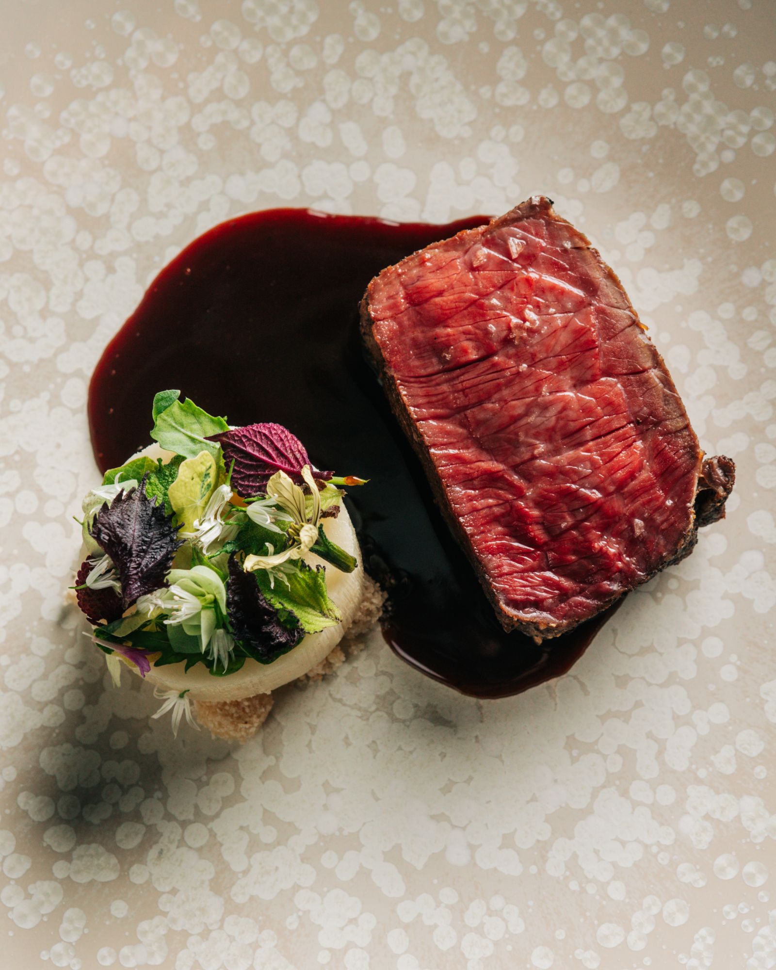 Plated beef dish with red wine reduction and edible flowers at Nic + Junior’s, an elevated River North dining experience in Chicago.