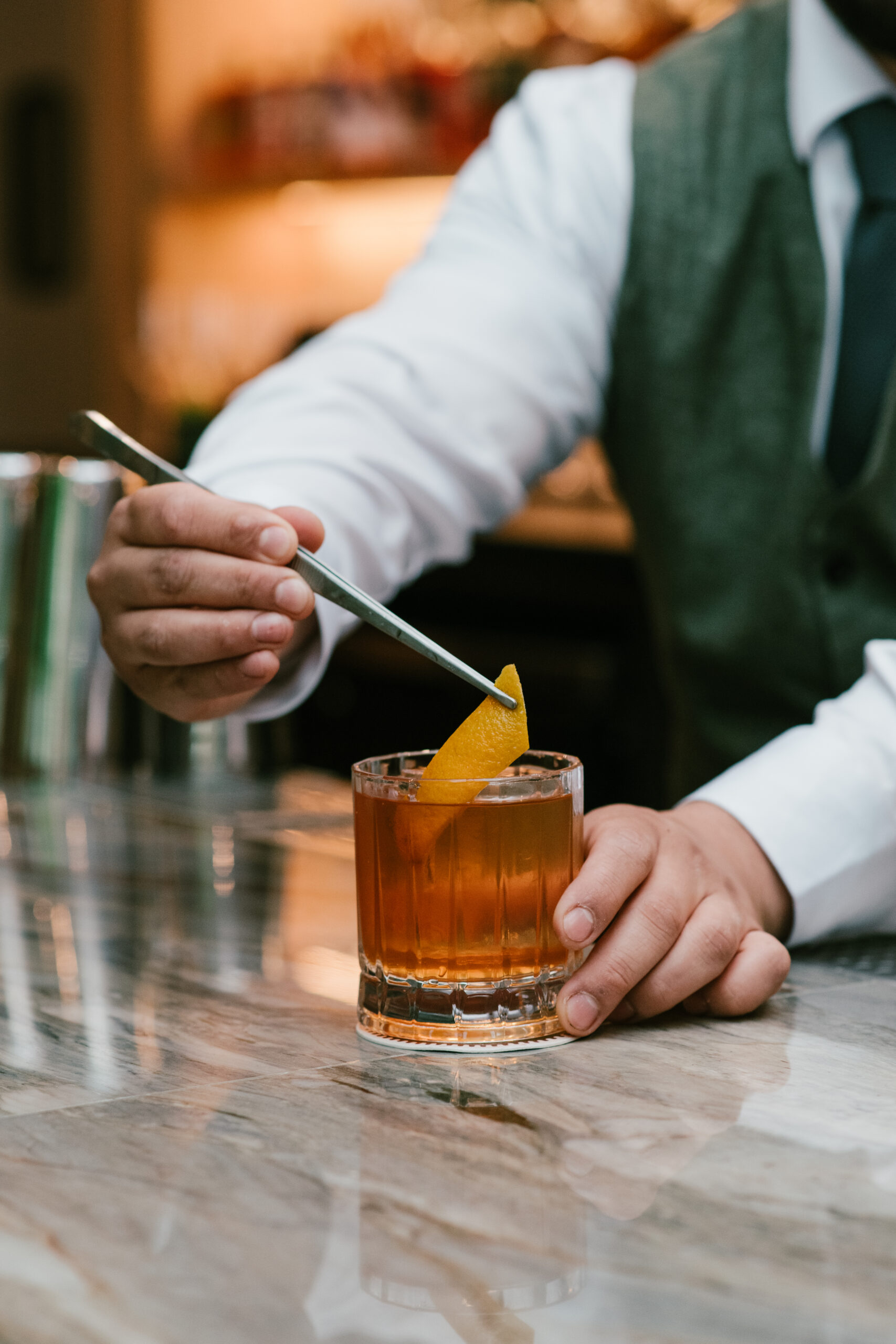 Bartender at Nic + Junior’s garnishing a cocktail with a fresh orange twist, highlighting the craft and care behind the River North cocktail experience.
