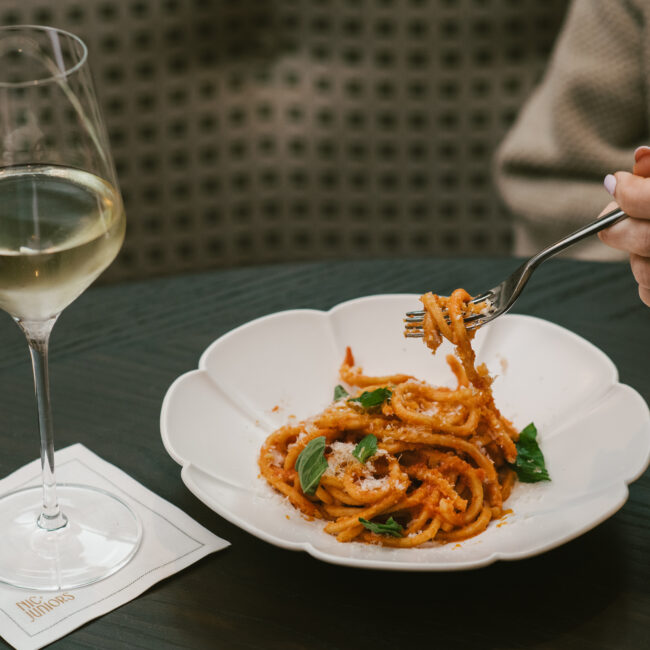 A forkful of spaghetti in tomato sauce with basil and parmesan, served with a glass of white wine at Nic + Junior’s in River North