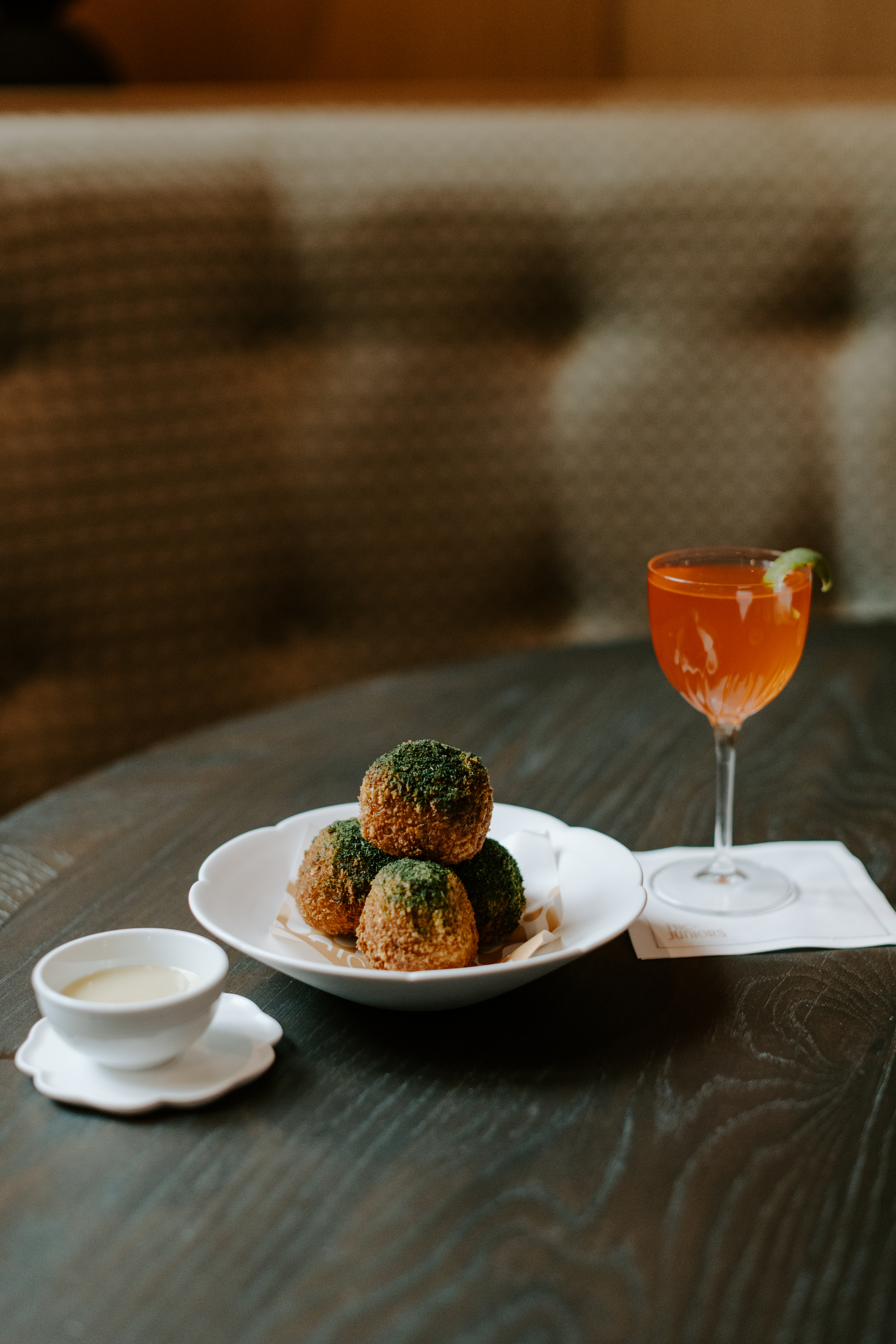 Fried croquettes with dipping sauce and a vibrant cocktail at Nic + Junior’s in River North, Chicago