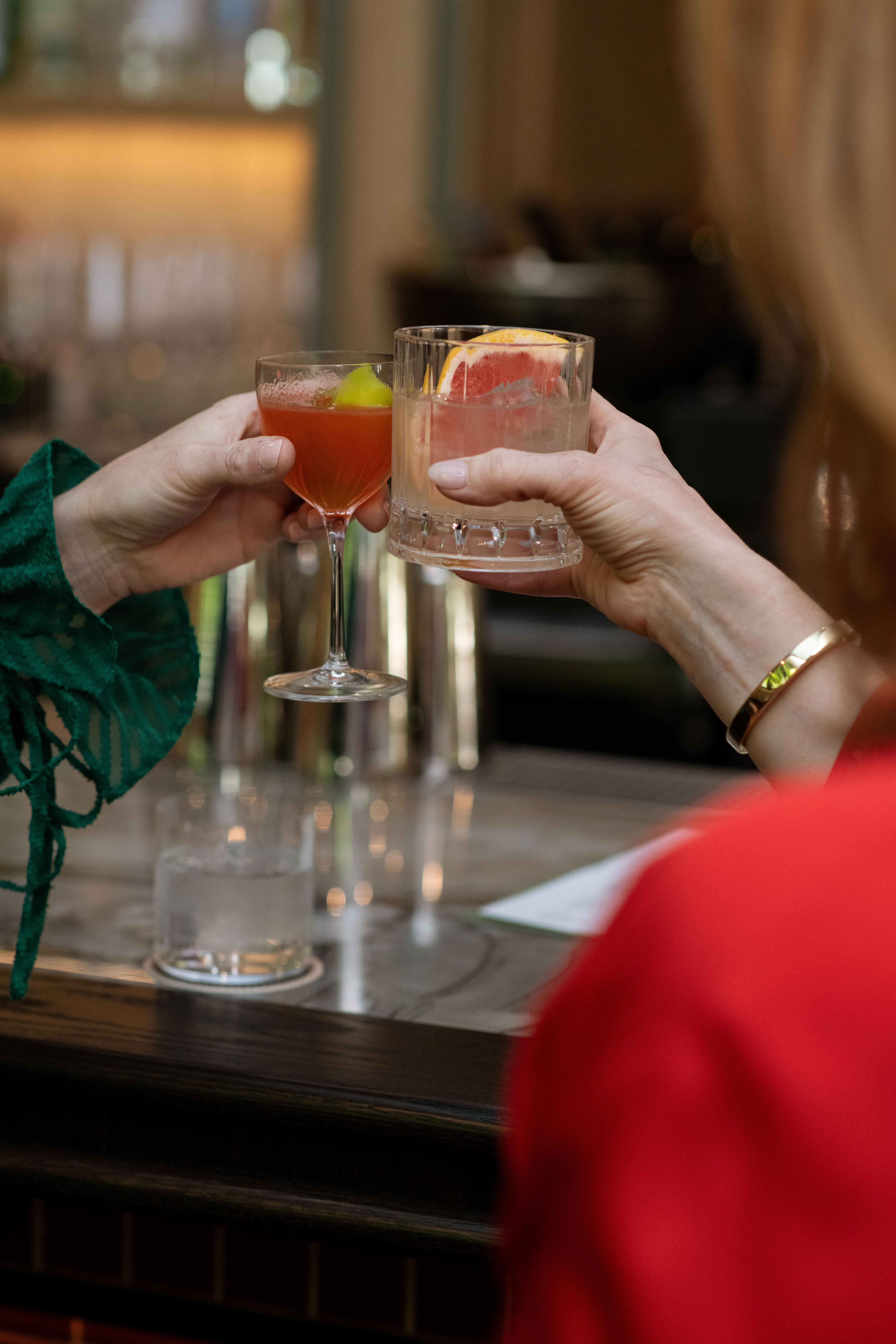 Two guests clinking cocktails at the bar at Nic + Junior’s in River North, Chicago