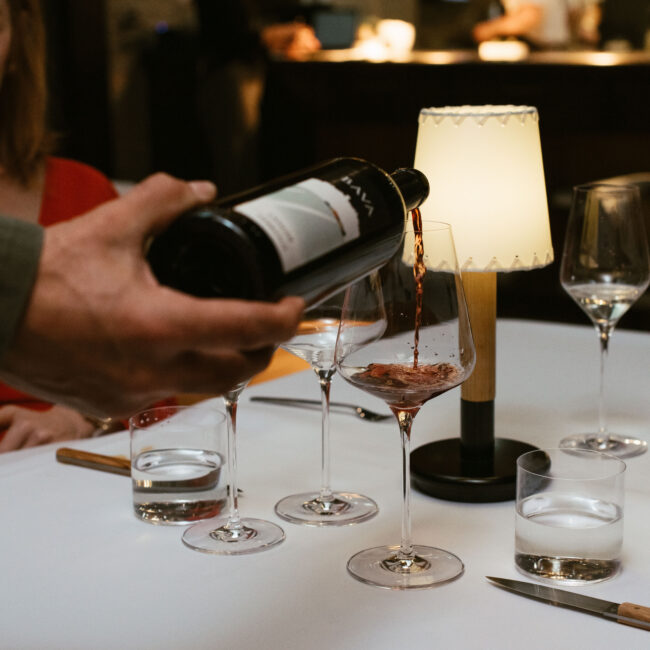 Server pouring red wine into a glass at Nic + Junior’s in River North, Chicago during dinner service