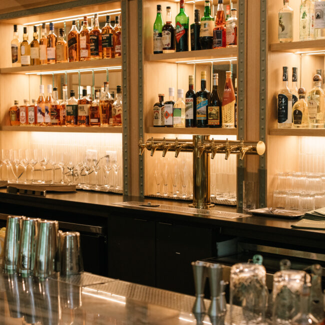 Warmly lit bar at Nic + Junior’s, stocked with spirits and cocktail tools, ready for evening service