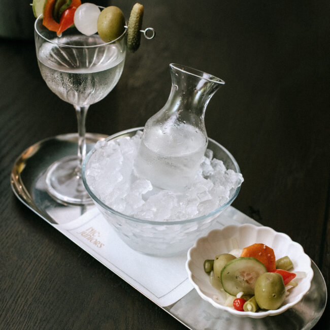 Martini served at Nic + Junior’s with a creative salad-style garnish, photographed on a dark wood table
