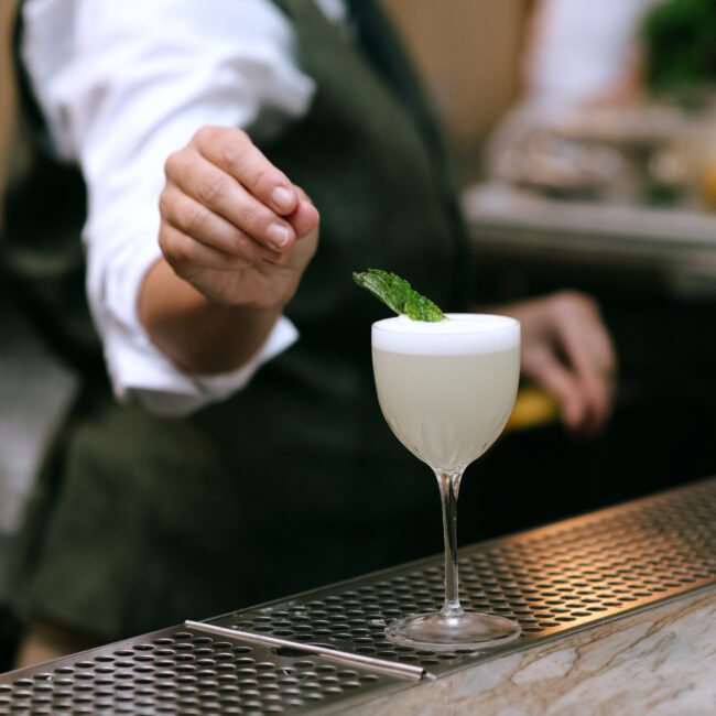 Bartender garnishing a Southside cocktail with fresh mint at Nic + Junior’s bar